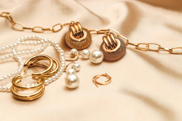 Assorted gold and pearl jewelry pieces, including hoop earrings, pearl studs, and a chain necklace, arranged on beige satin fabric.