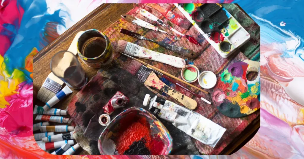 Top view of colorful acrylic painting supplies including brushes, paint tubes, palette, and mixing tray on a wooden table with a vibrant background